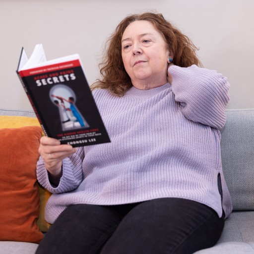 Woman sat down reading a book, holding her neck