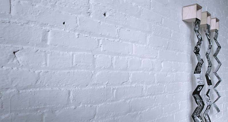 A photo of a white brick wall and on it there are some wood boxes with some zig zag paper flyers popping from them.