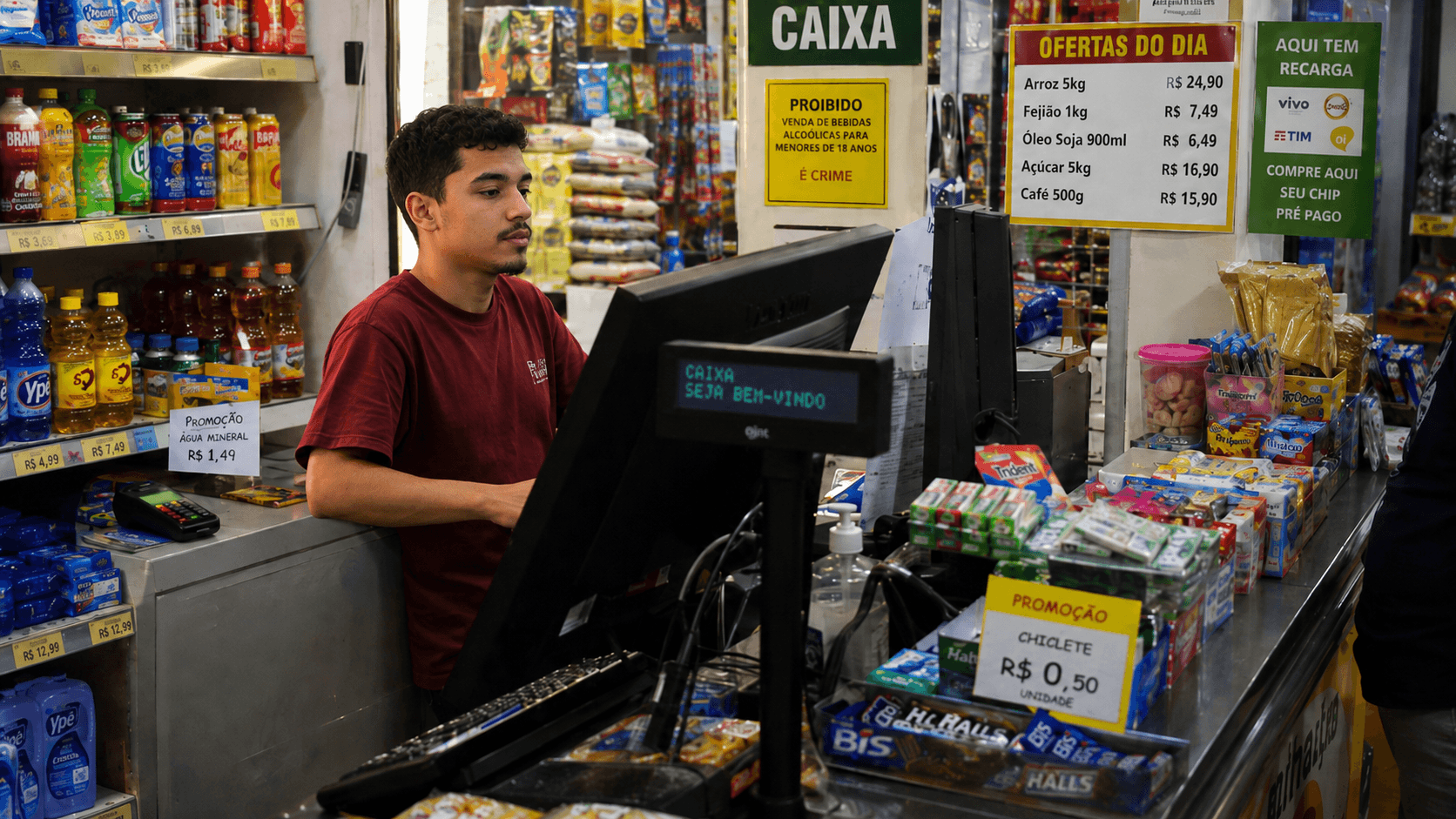 Jovem vendedor trabalhando no caixa do PDV de uma loja, registrando uma venda.