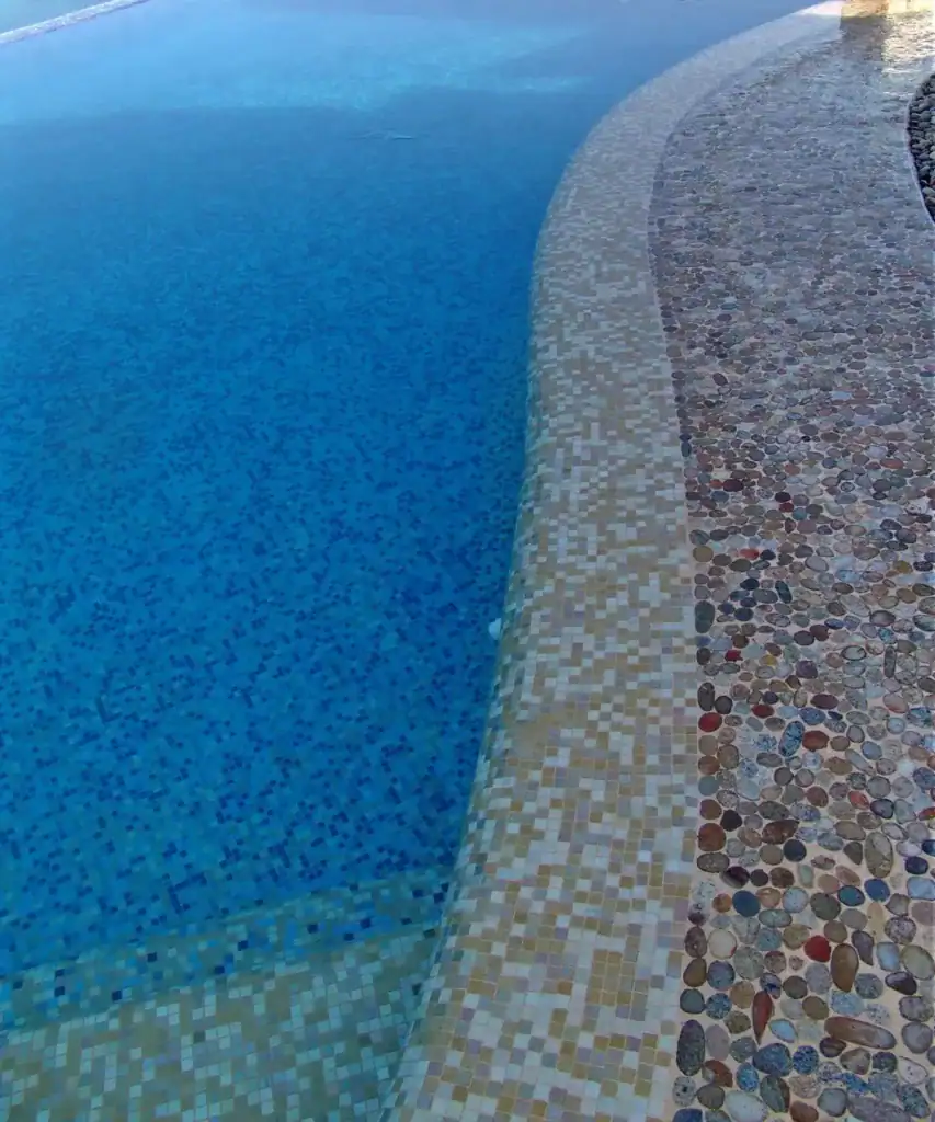 River rock coping set at the edge of a mosaic pool — Mosaiclegs Art Studio