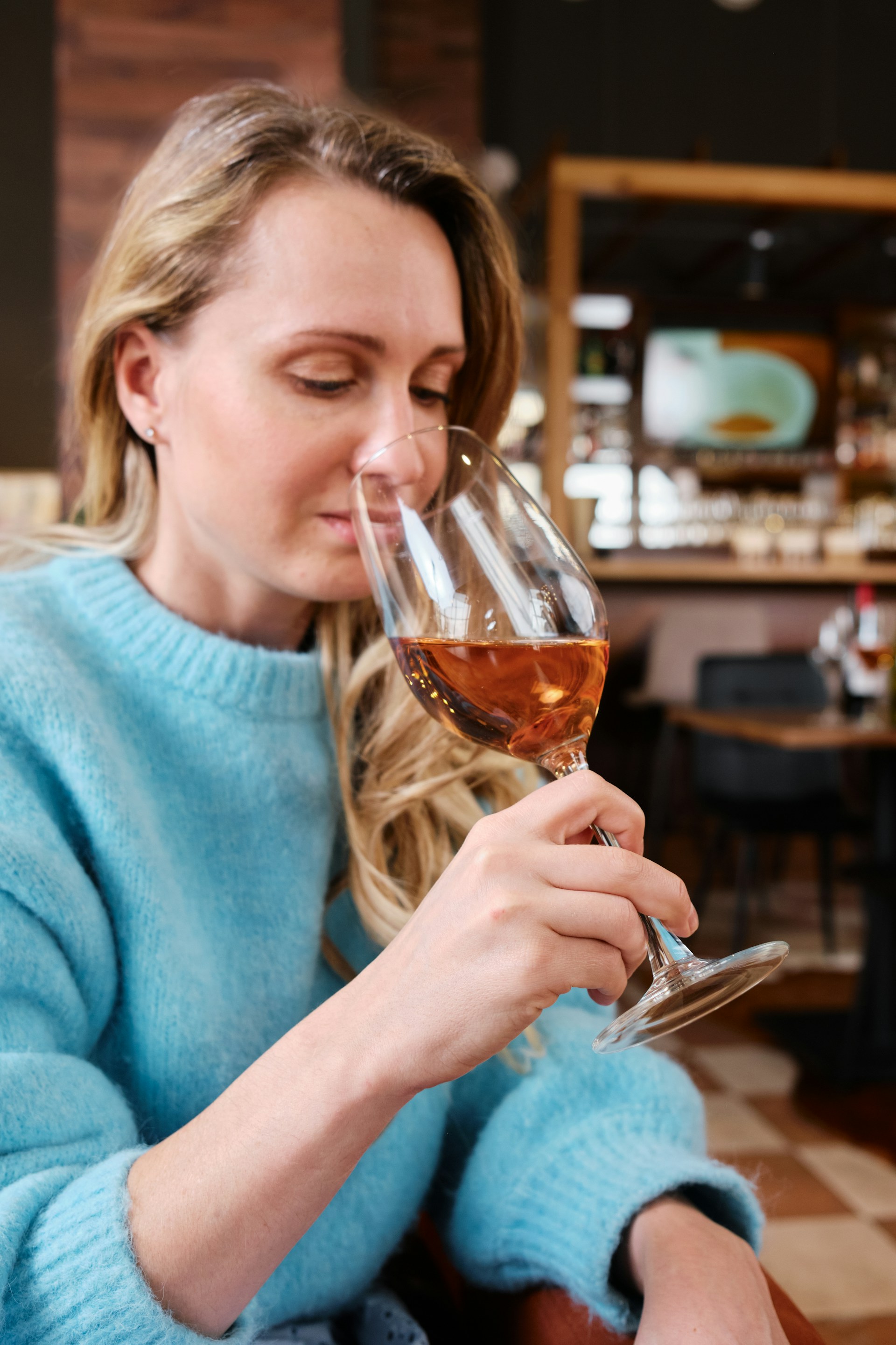 Smiling young woman with curly hair sitting at a laptop, in front of a teal wall.