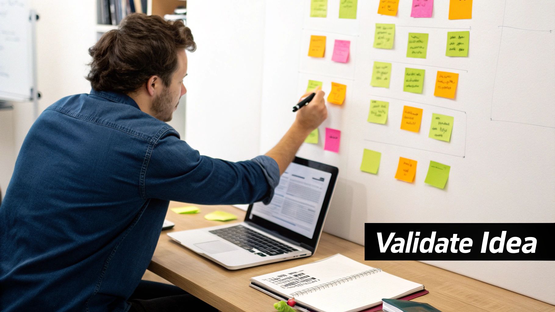 Man organizing ideas on a whiteboard with colorful sticky notes, a laptop, and a notebook.