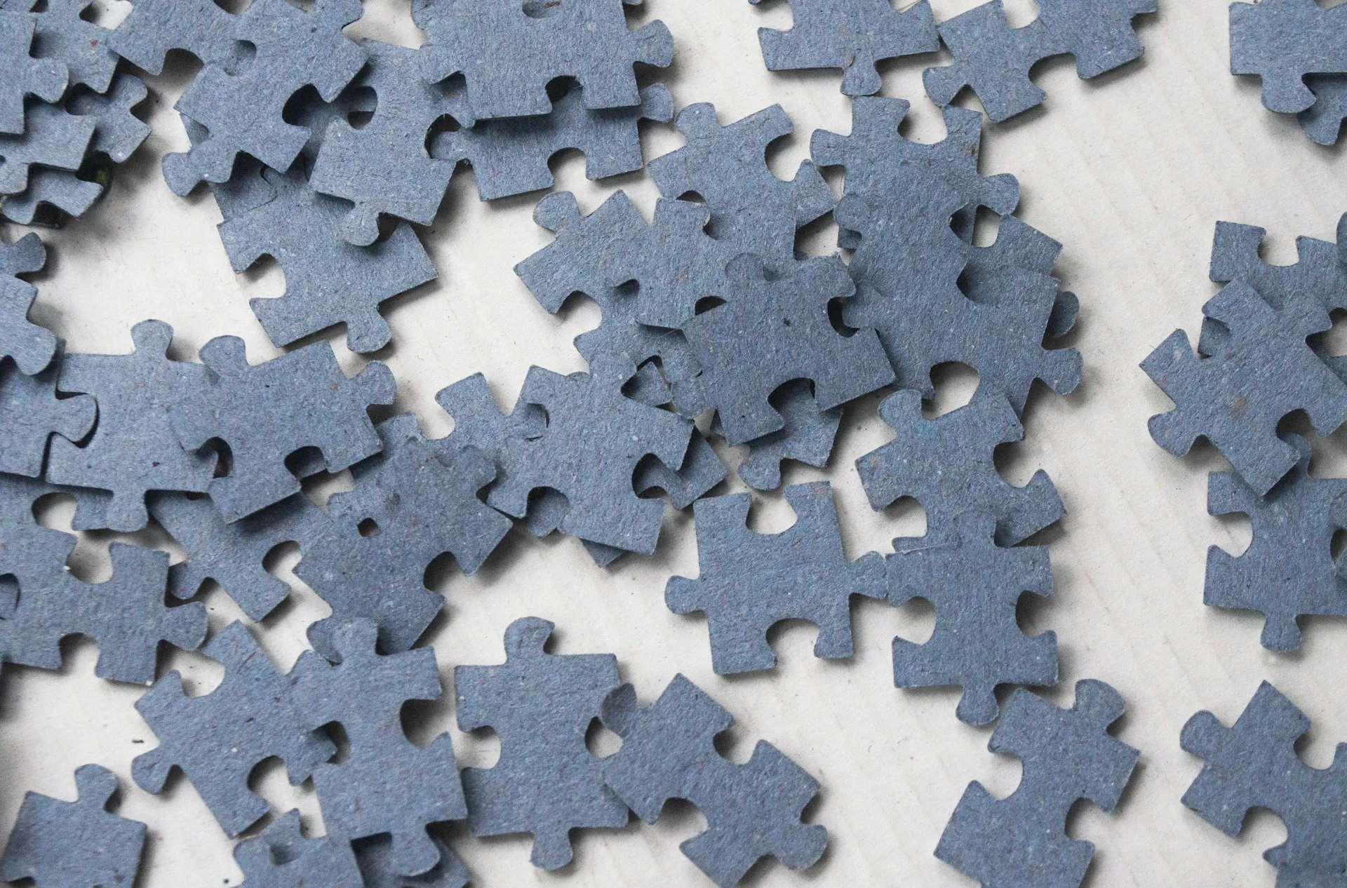 Close-up of dark blue puzzle pieces scattered on a white surface, symbolizing problem-solving and critical thinking for high school students in RISE Research STEM programs.