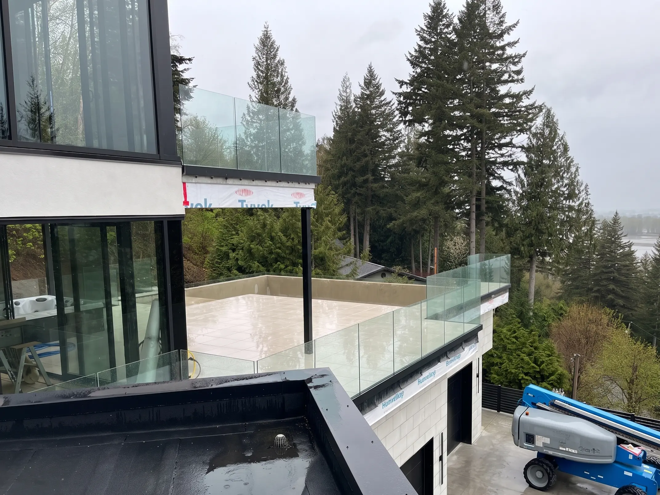 Frameless glass railings on multiple balconies of a modern Vancouver Island home backed by coastal evergreen forest