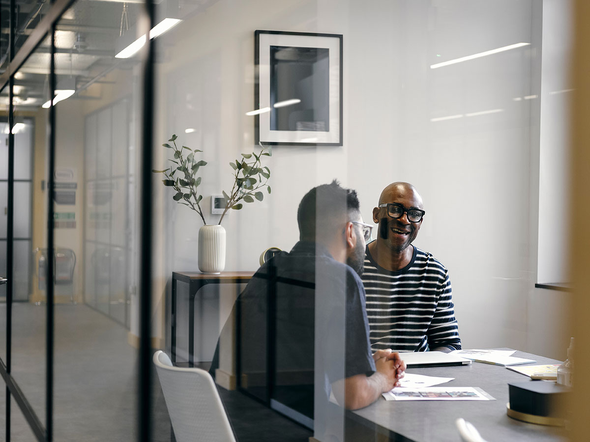 Two men sat inside a glass walled office