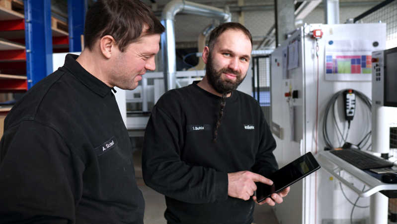 Two carpenters are serving a tablet in furniture production.