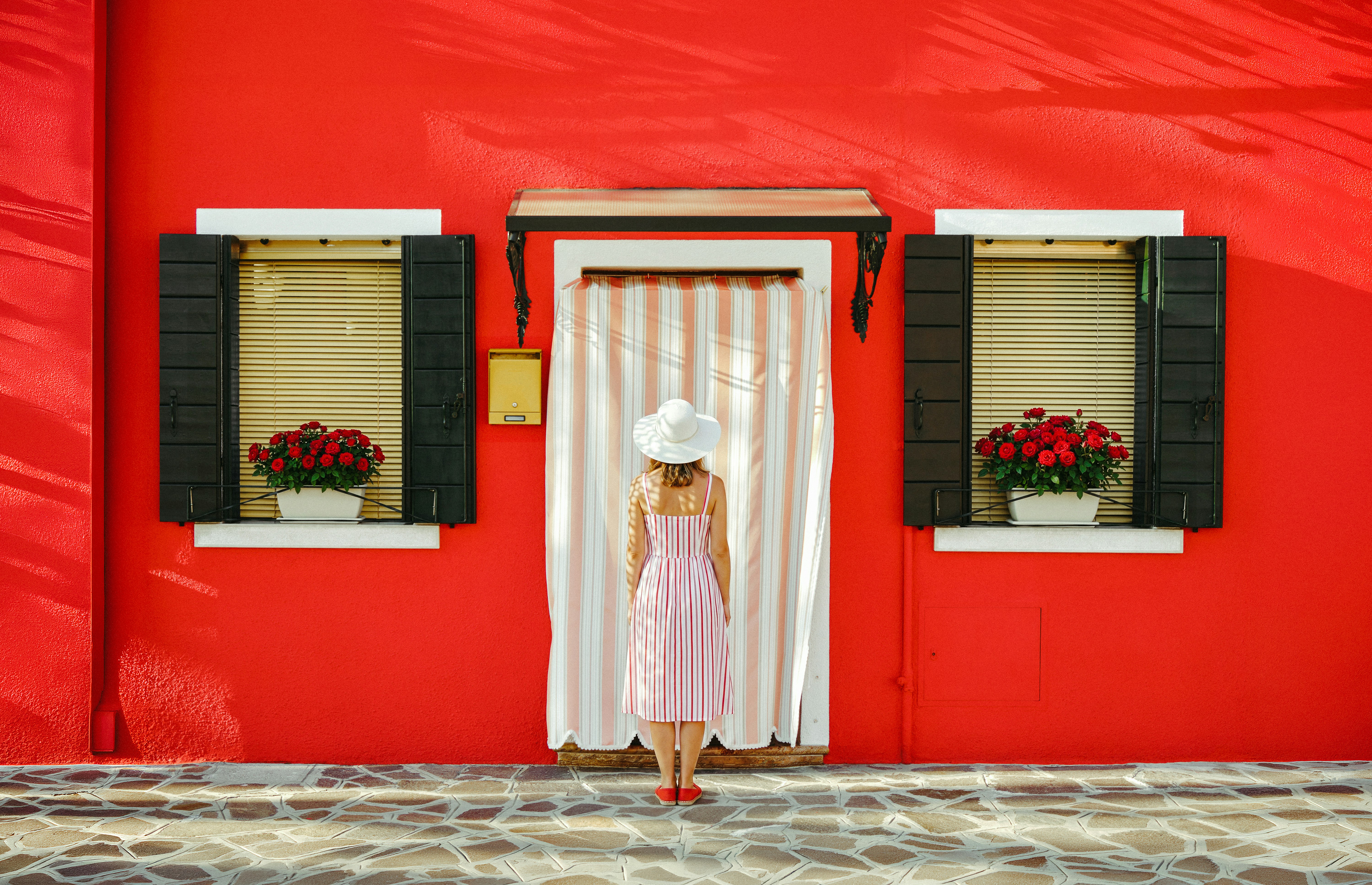 Woman in dress stands before bright red building