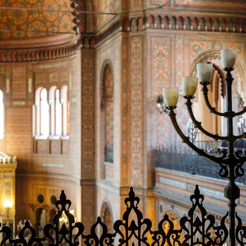 Ornate interior of a historical building with detailed decoration, arched windows, and a decorative candelabra in the foreground.
