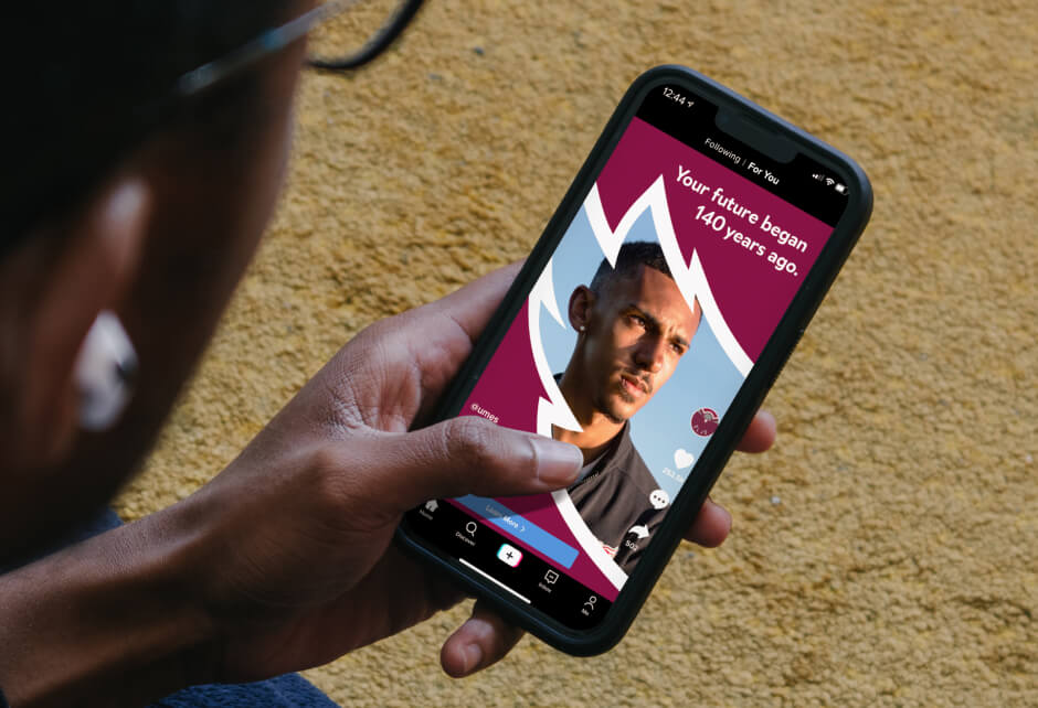 A person holding a smartphone displays an app showing a man's face and the text, Your future began 140 years ago, capturing the brand core truth against a maroon and white background.