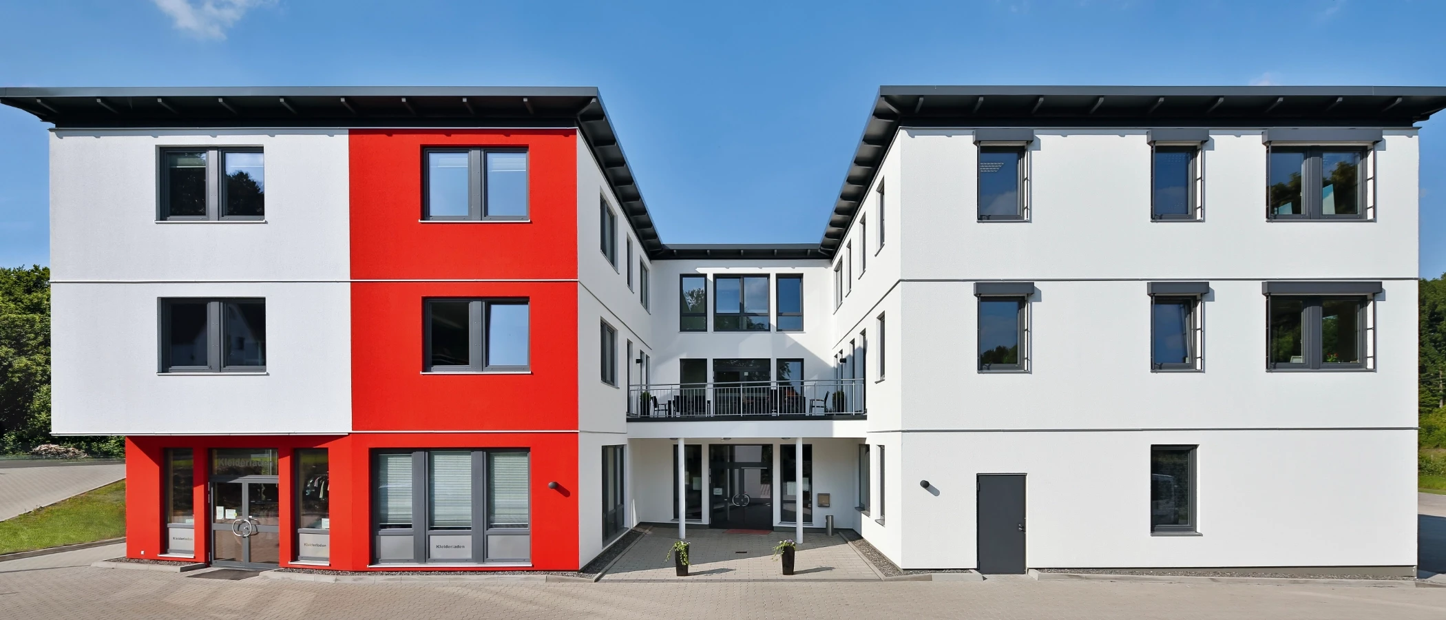 Modernes dreistöckiges Gebäude mit weißer und leuchtend roter Fassade, vielen Fenstern und einem Flachdach.