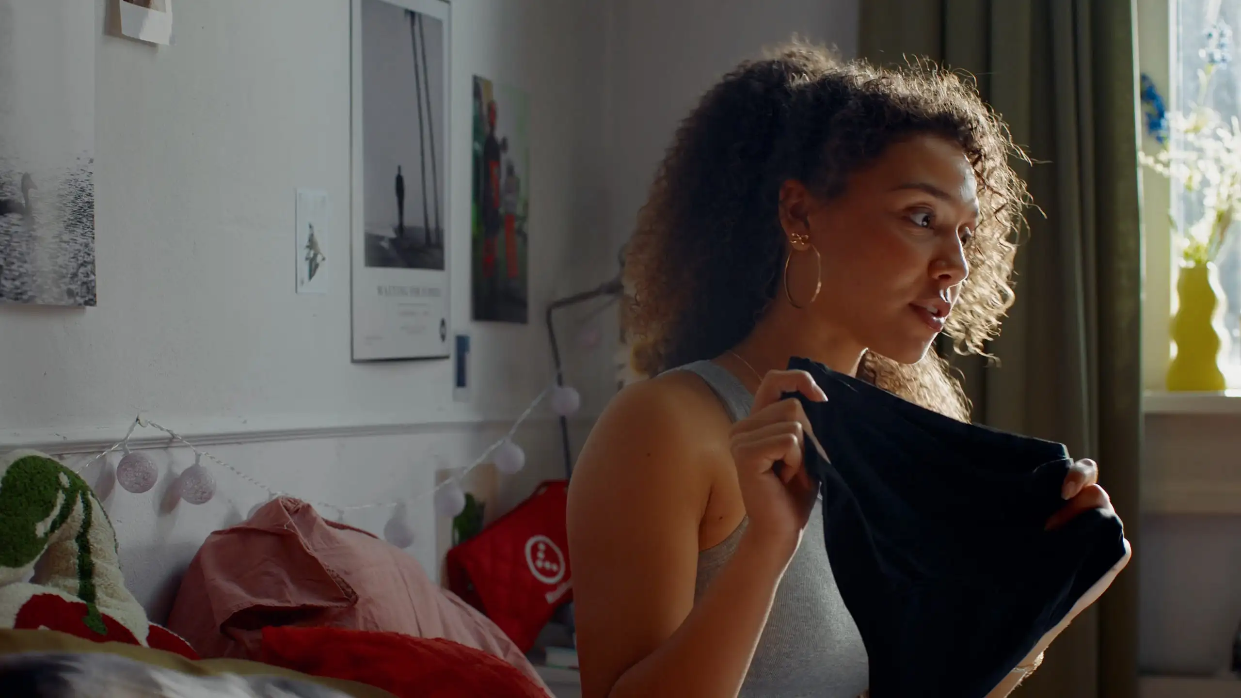 Close up of a young woman inspecting a dark garment, caught mid sentence in her bedroom.