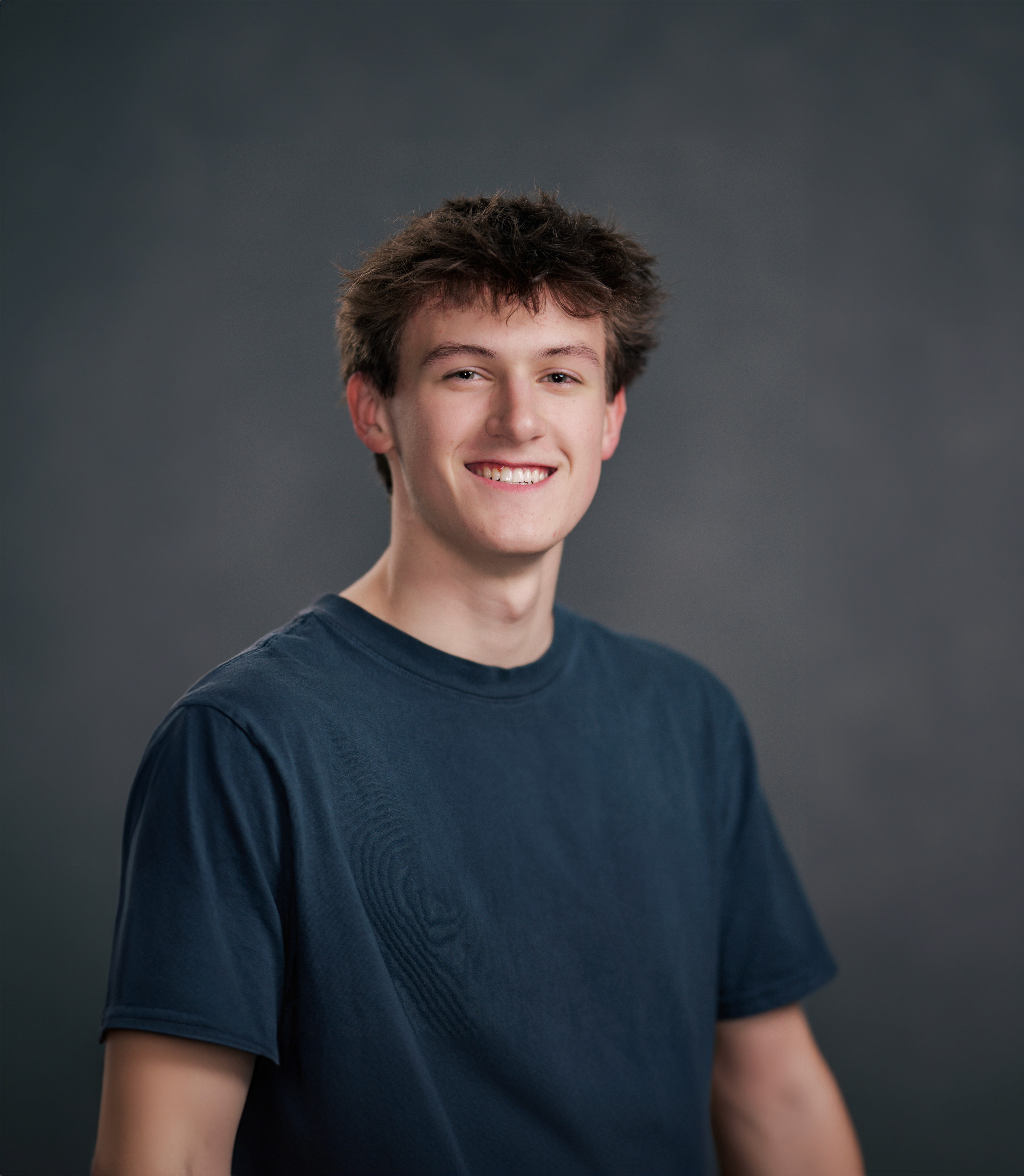 A person wearing headphones sits at a desk with a large curved monitor displaying graphic design software, surrounded by a laptop, smartphone, and potted plant, creating a modern workspace setup.