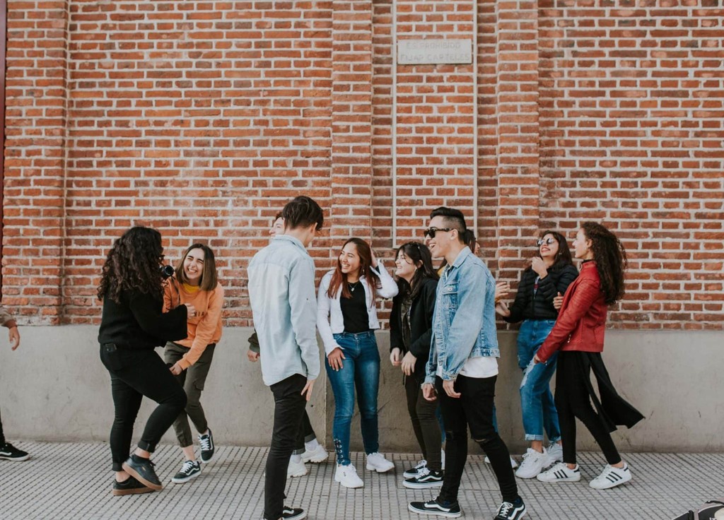 Group of happy young adults laughing together outside against a brick wall.