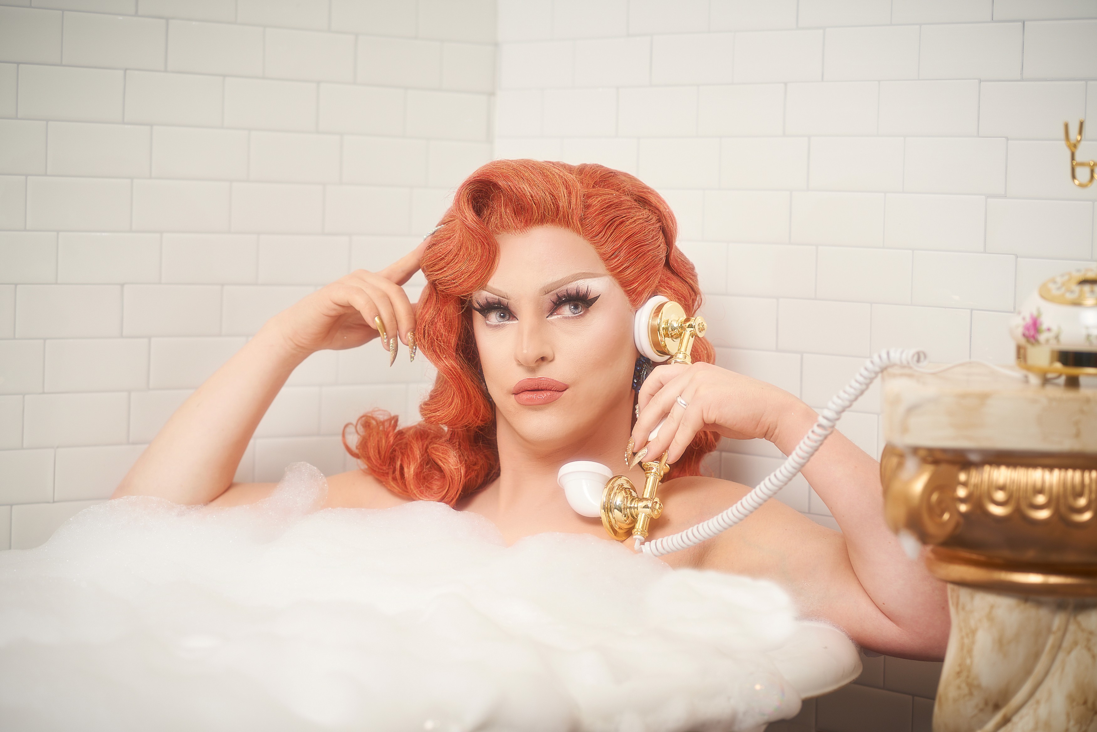 Miz Cracker reclining in a foam filled bathtub with a vintage telephone
