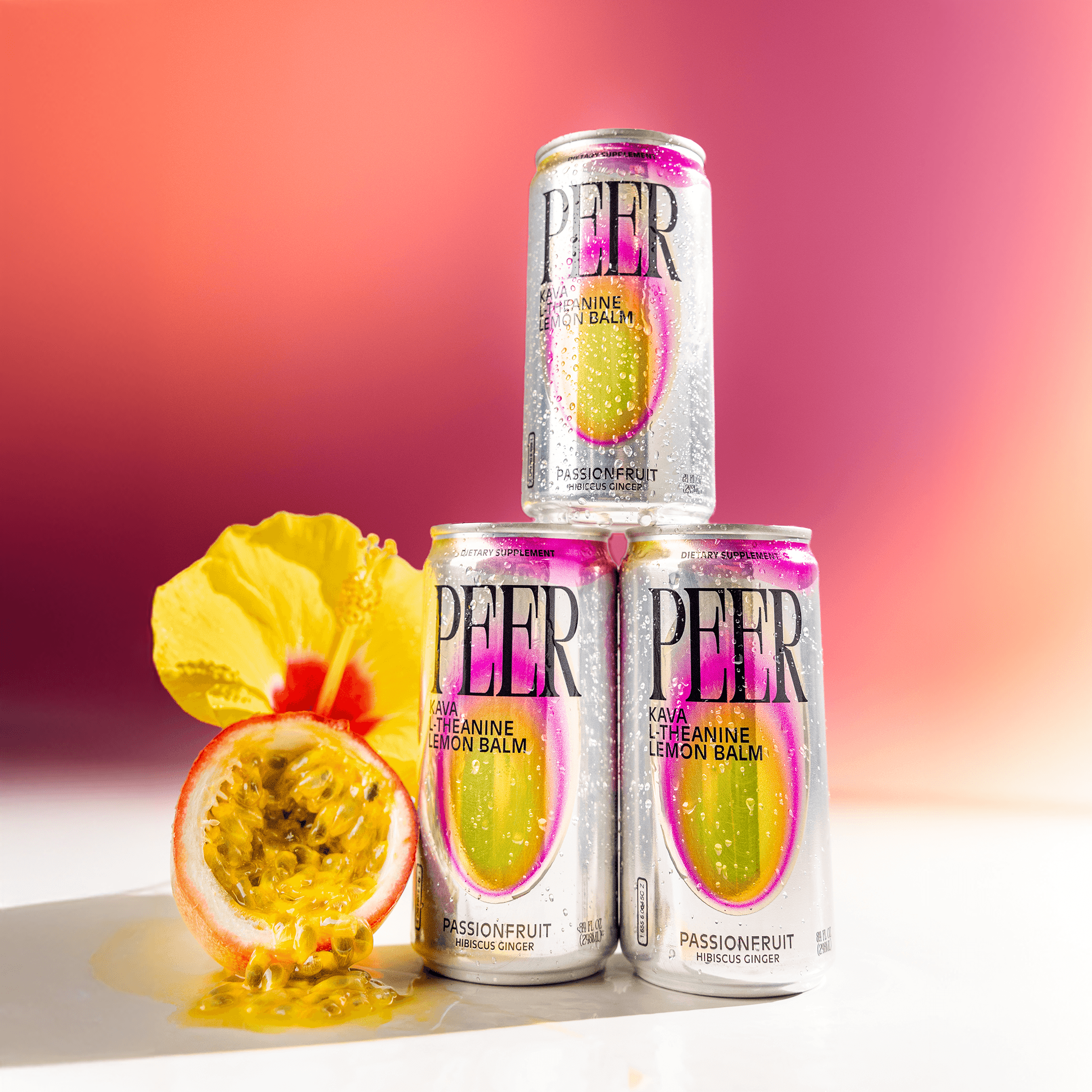 Three silver cans of PEER balm with pink and yellow graphics are arranged in a pyramid on a white surface, with a cut passionfruit and a yellow flower beside them against a pink-to-orange gradient background.