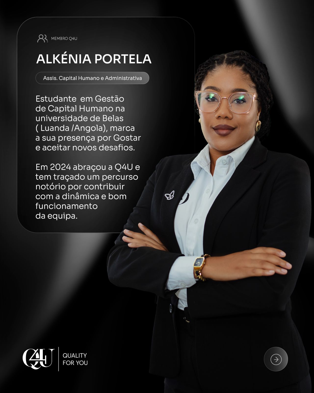 A woman with long red hair in a black sleeveless top smiles warmly. She stands in a softly lit room, conveying a cheerful and welcoming mood.