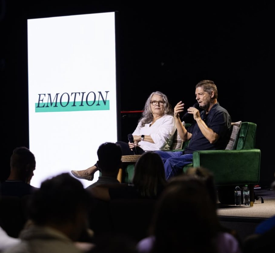 Dr. Glenn and Phyllis Hill on stage in front of a screen reading EMOTION