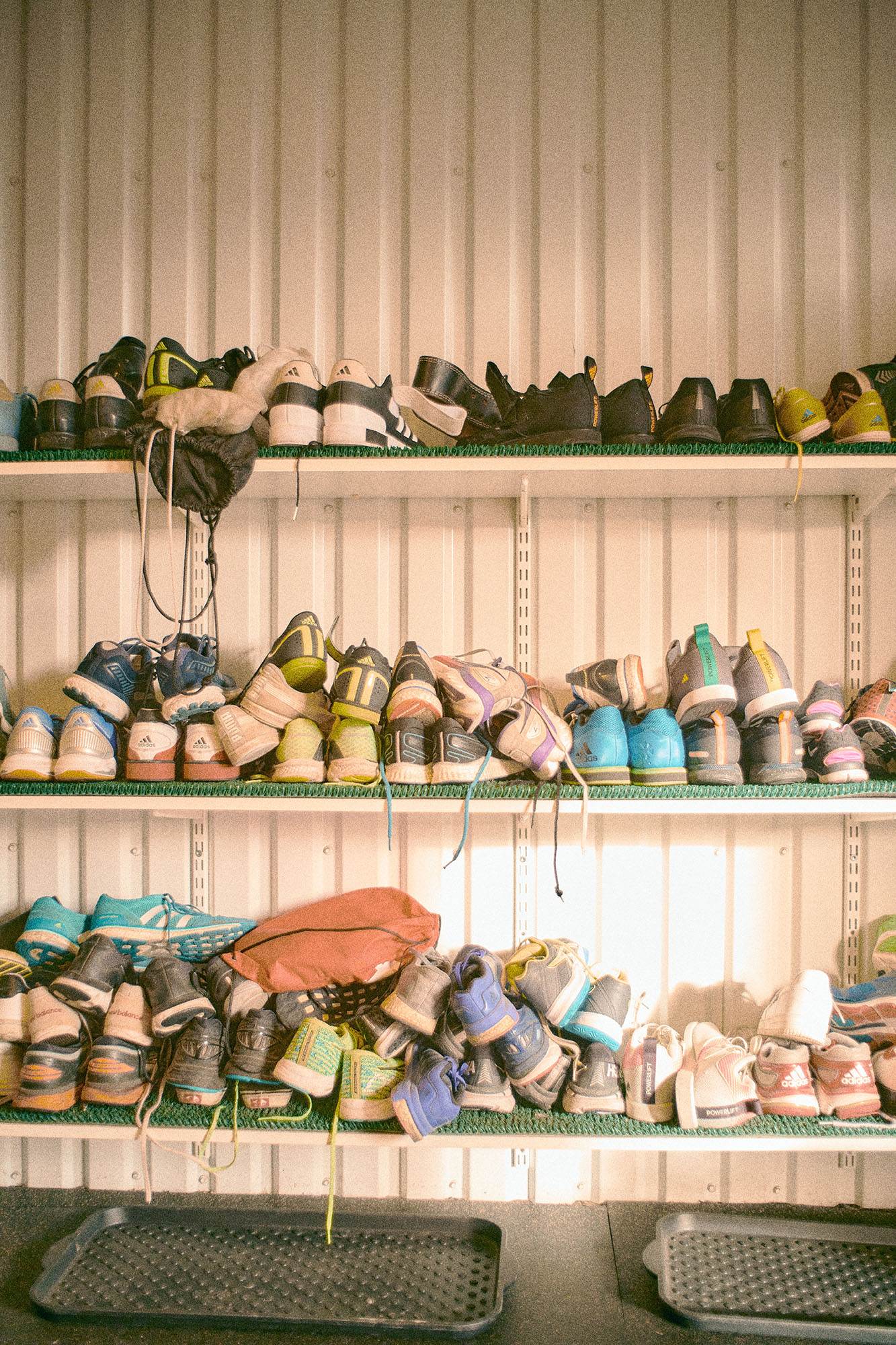 Många skor som står huller om buller på tre hyller som sitter över varandra.