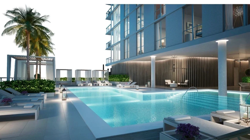Poolside amenity area of a North Bay Village residential tower, with a rectangular pool, white cabanas, sun loungers, palm trees, and a green privacy hedge.