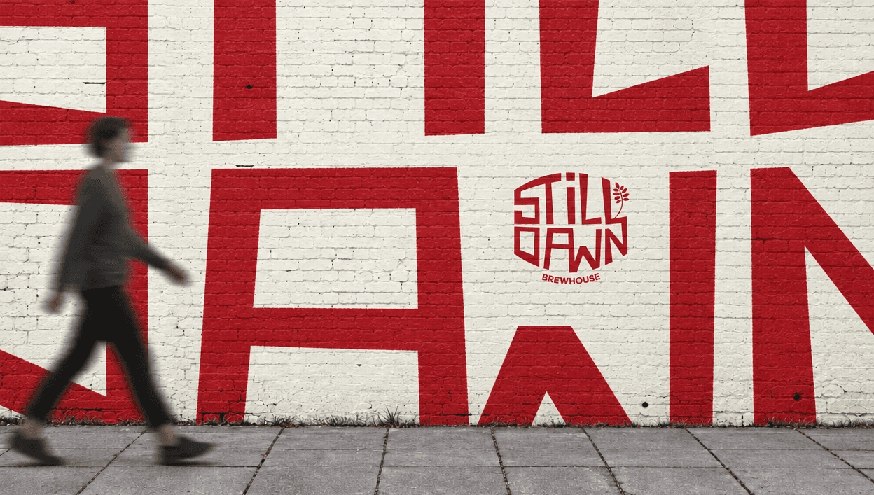 Oversized red Still Dawn mural painted across a white brick wall as a person walks past.