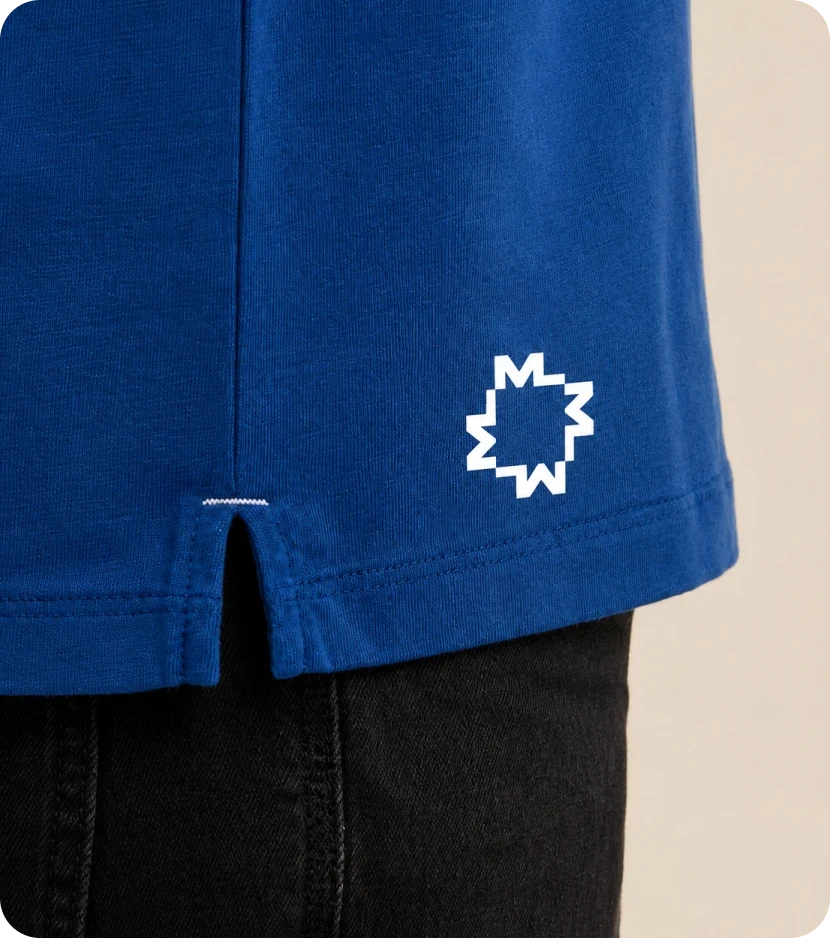 The white star-M symbol printed near the split hem of a cobalt blue T-shirt.