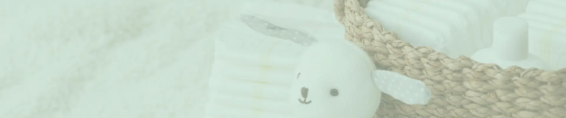 Wicker basket filled with baby diapers, lotion, and a white stuffed bunny with polka dot ears, placed on a fluffy white surface