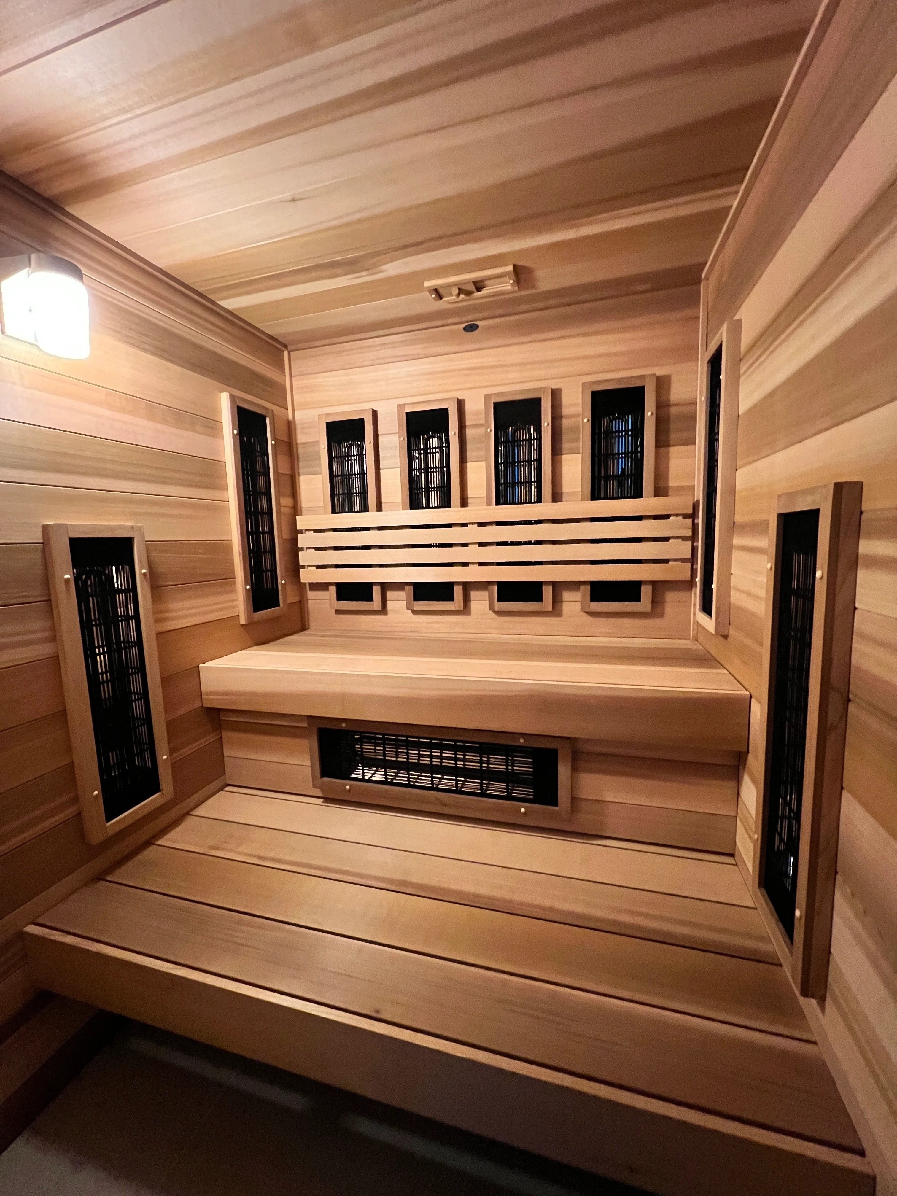 Wood-lined infrared sauna with a bench and black heating panels mounted in the walls and beneath the seat.