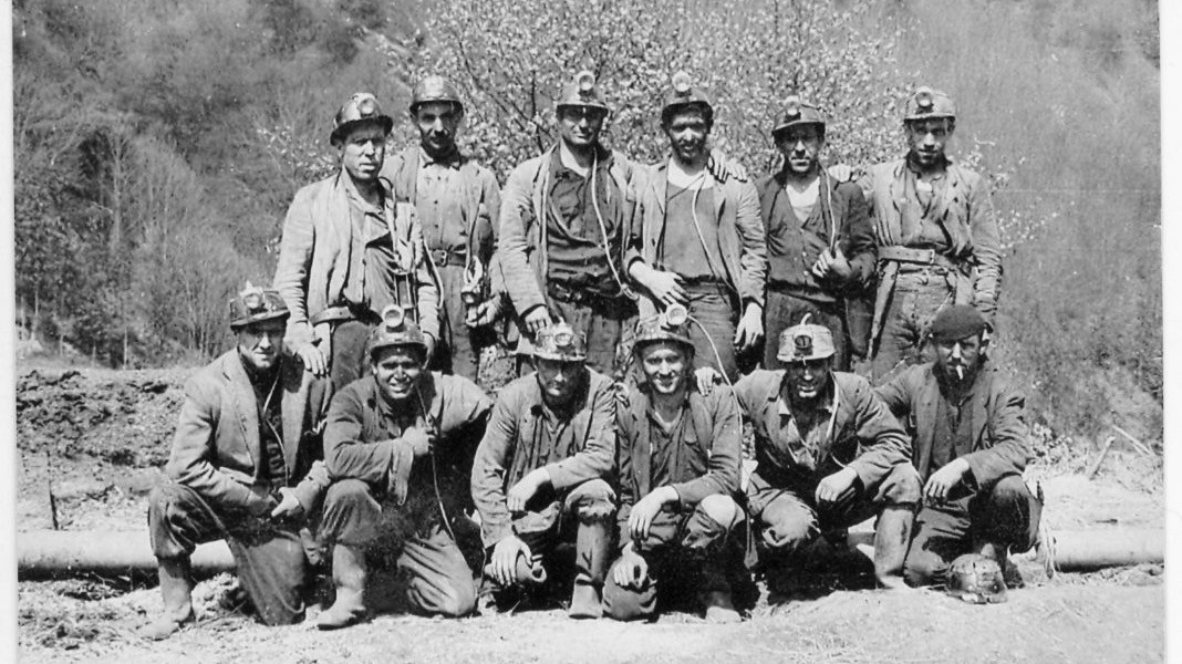 Groupe de mineurs en tenue de travail, posant devant une mine sur une photographie ancienne en noir et blanc.