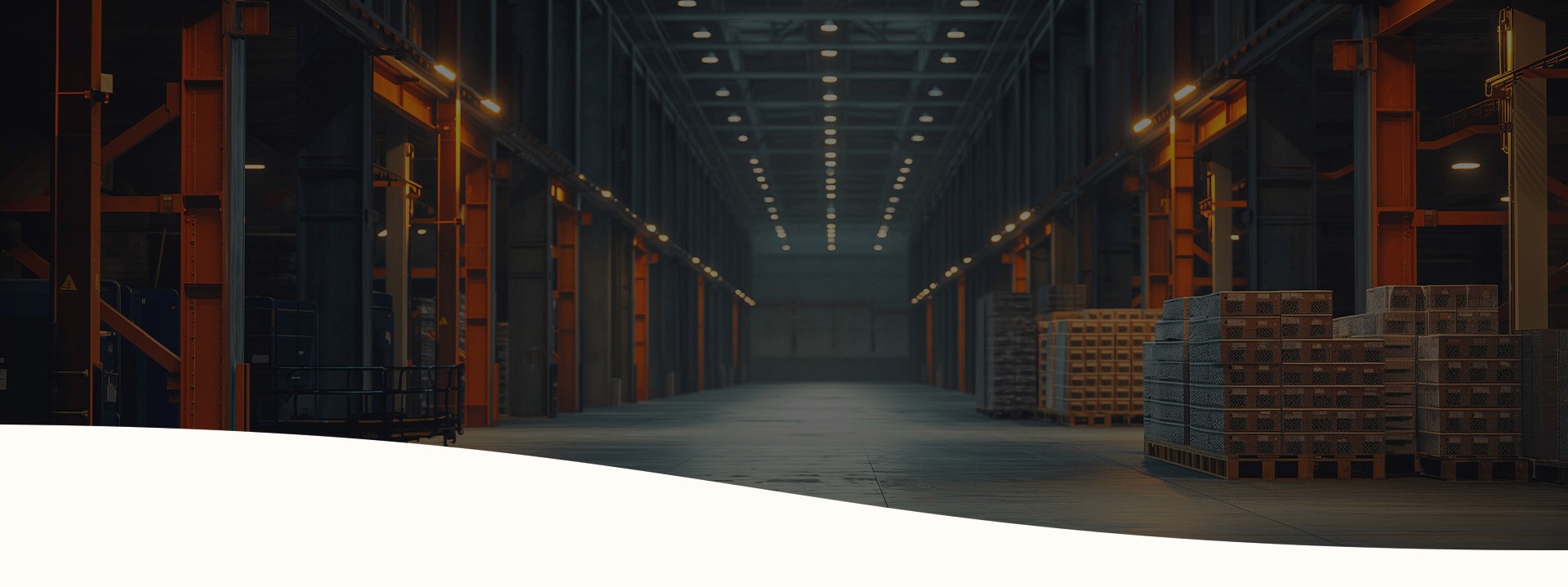 A warehouse. It has many orange parts. There are also stacks of wooden pallets in the background. Many lights are on.