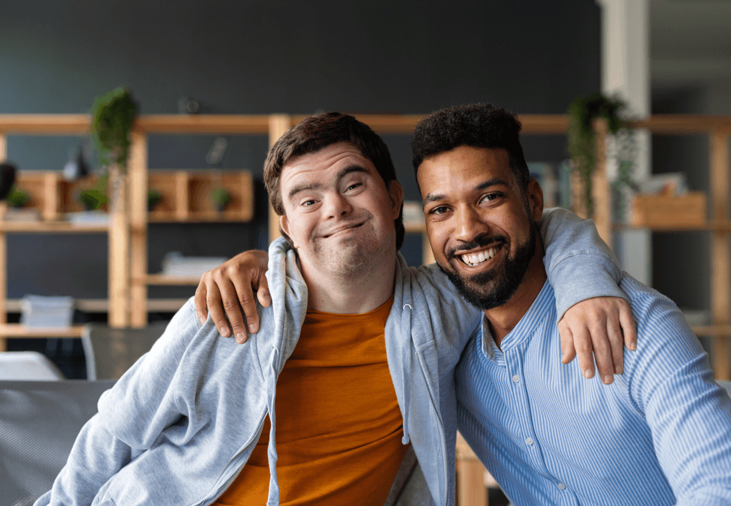 Grupo diverso de pessoas em pé, sorrindo e posando para a foto em frente a uma grande janela de escritório. A imagem transmite um ambiente acolhedor e colaborativo, refletindo a alegria e a união do grupo.