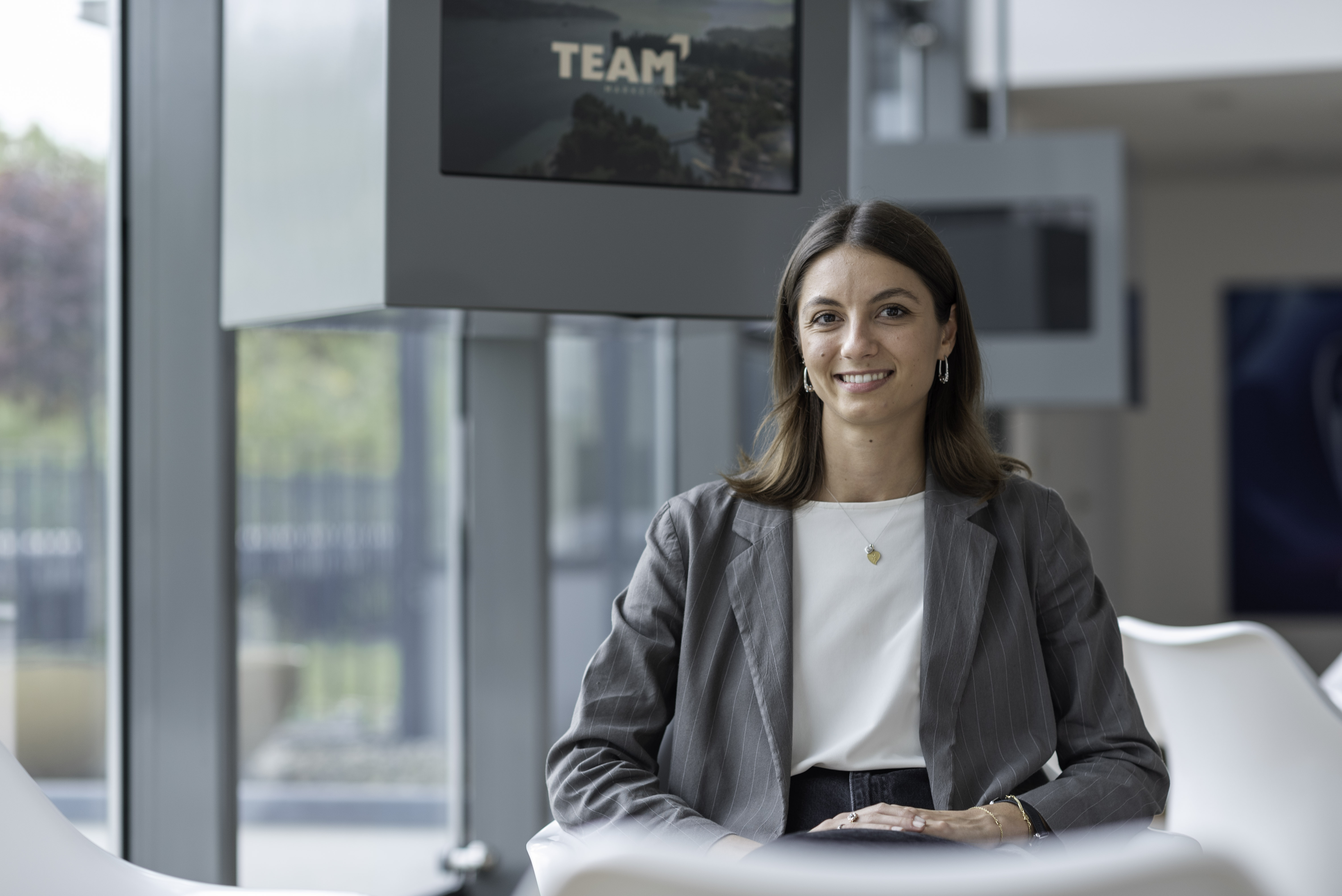 Female Team member seated confidently in a modern office space, with a Team logo visible in the background.