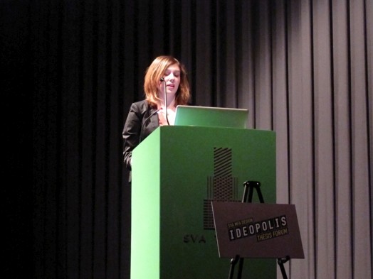 a woman is giving a speech from the green stand on the Ideopolis exhibition