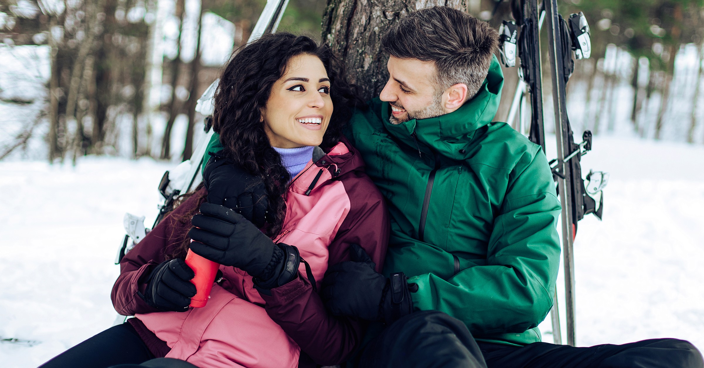 En man och en kvinna sitter tillsammans vid ett träd och tar en paus från att åka skidor.