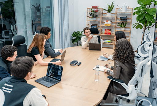 A diverse team of PointOne professionals collaborates around a light wooden table, actively discussing a digital product.