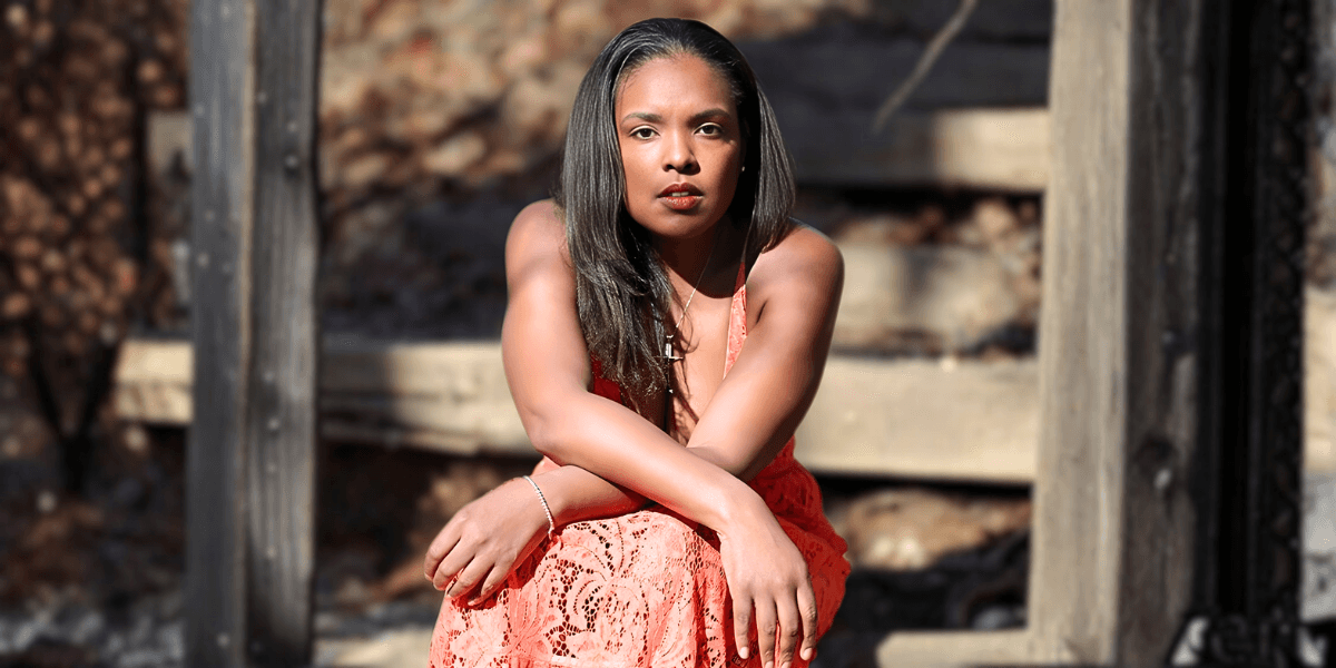 A woman in a red dress sits on a wooden bench, embodying strength and resilience, reflecting the spirit of Natalie Jean's music.