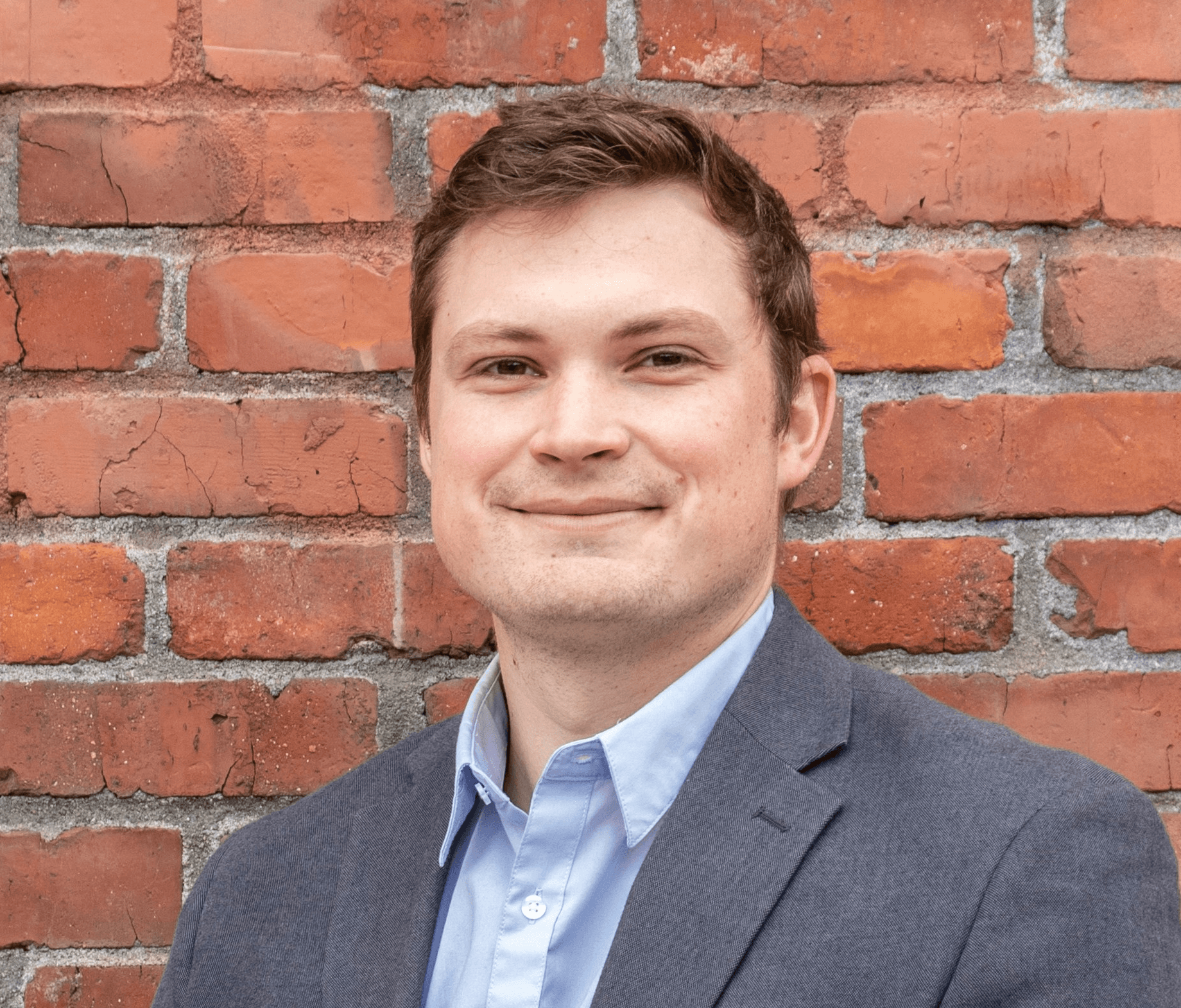 man in gray suit jacket standing beside brown brick wall