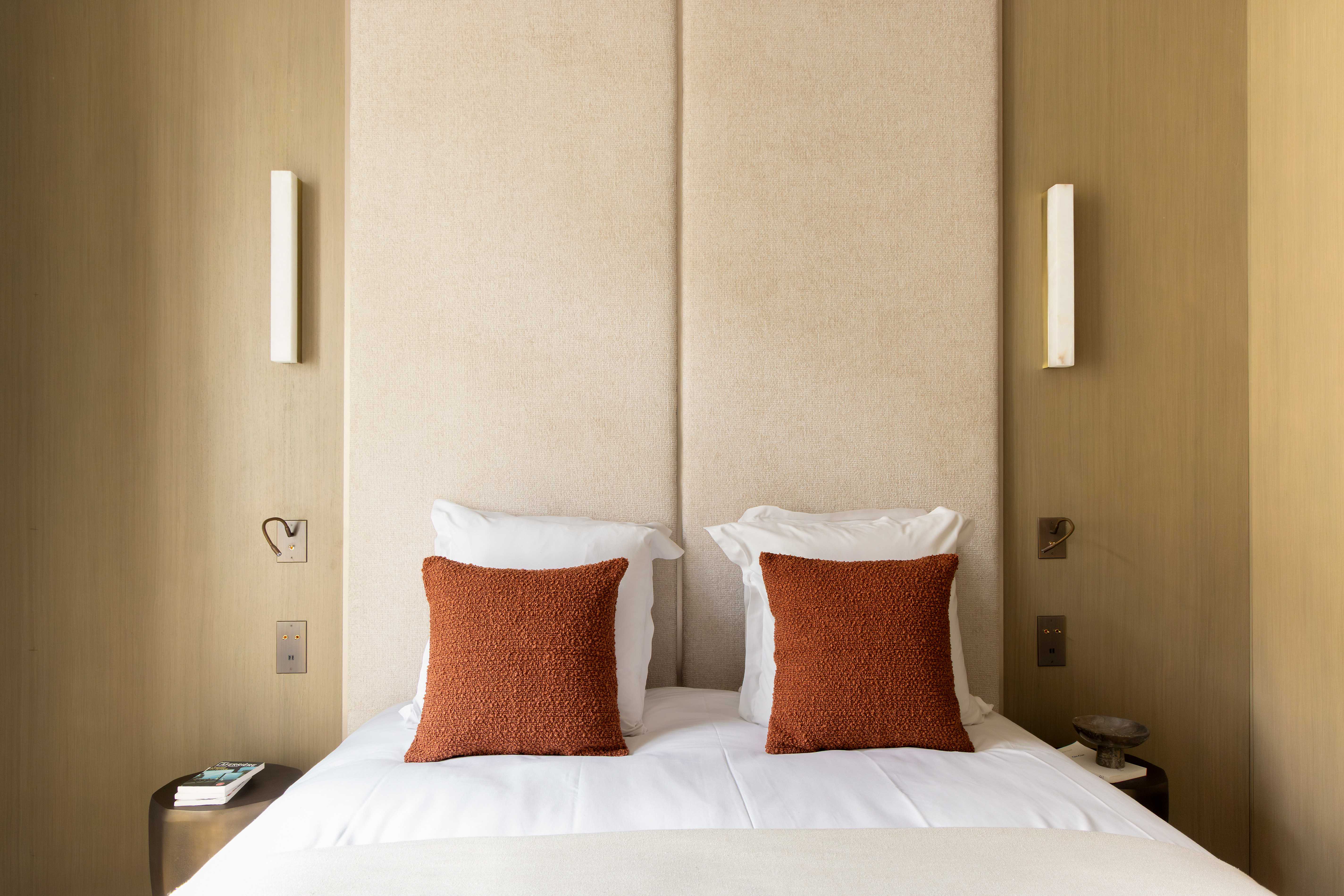 Gros plan tete de lit en velours sable avec coussins terracotta bouclettes et appliques en albatre dore