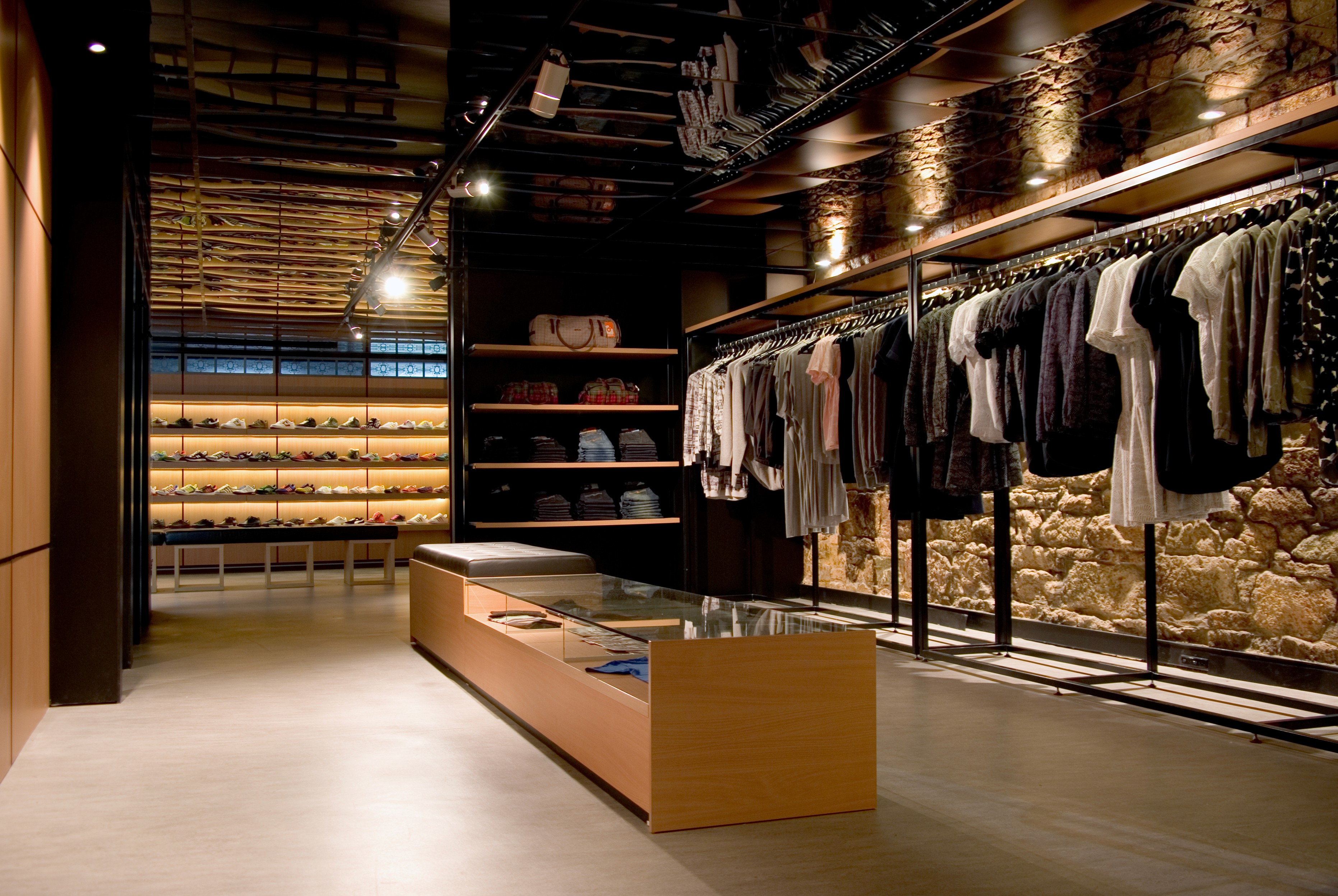 Interior view of Apartment Store with custom timber display tables, clothing rails against original stonework, and warm directional lighting.