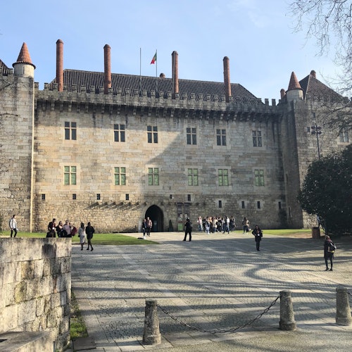 一座歷史悠久的石城堡，擁有幾個塔樓和一個中央庭院，人們在那裡走動和聚集。