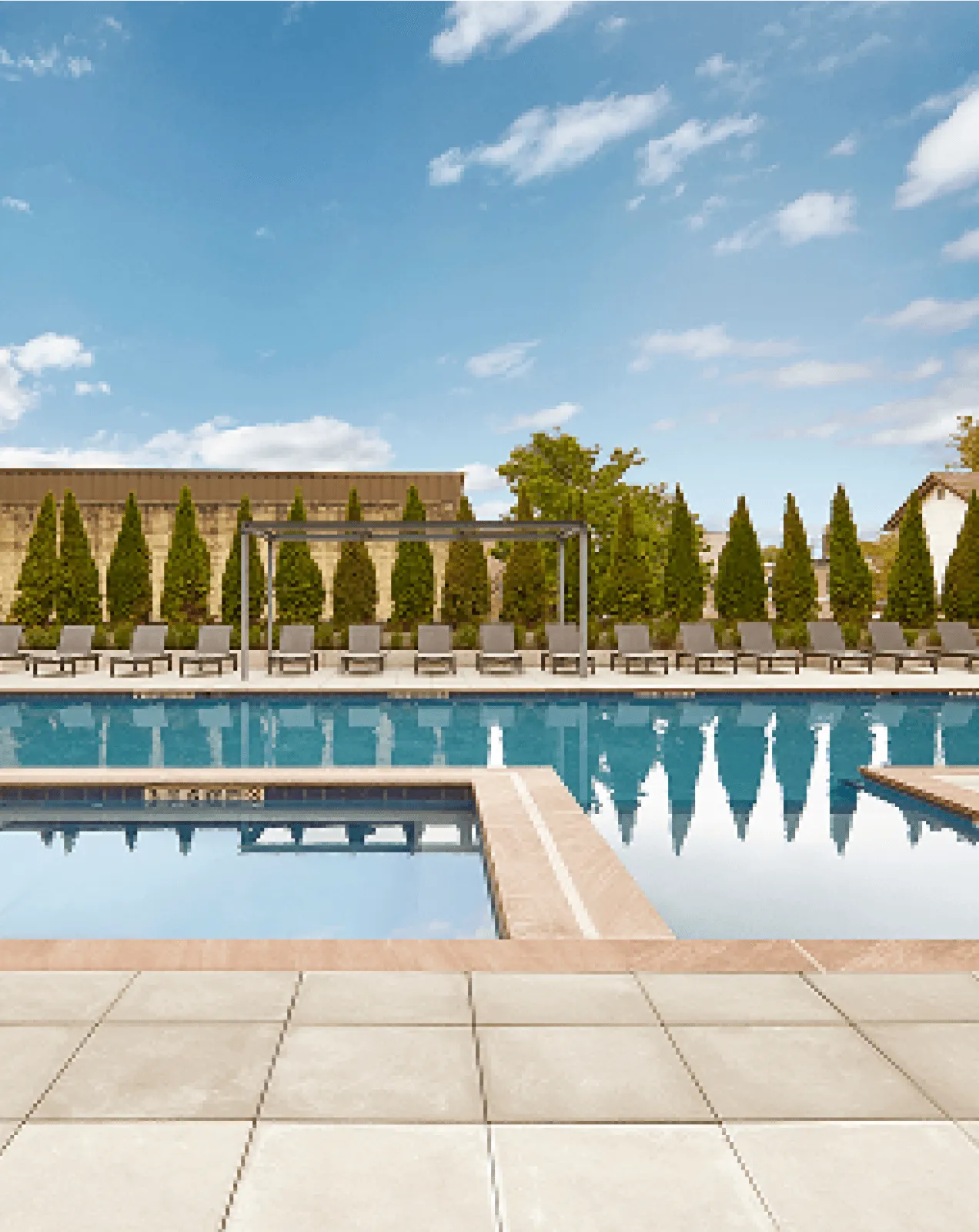 A tranquil outdoor swimming pool with clear blue water, surrounded by trees and a sunny sky.