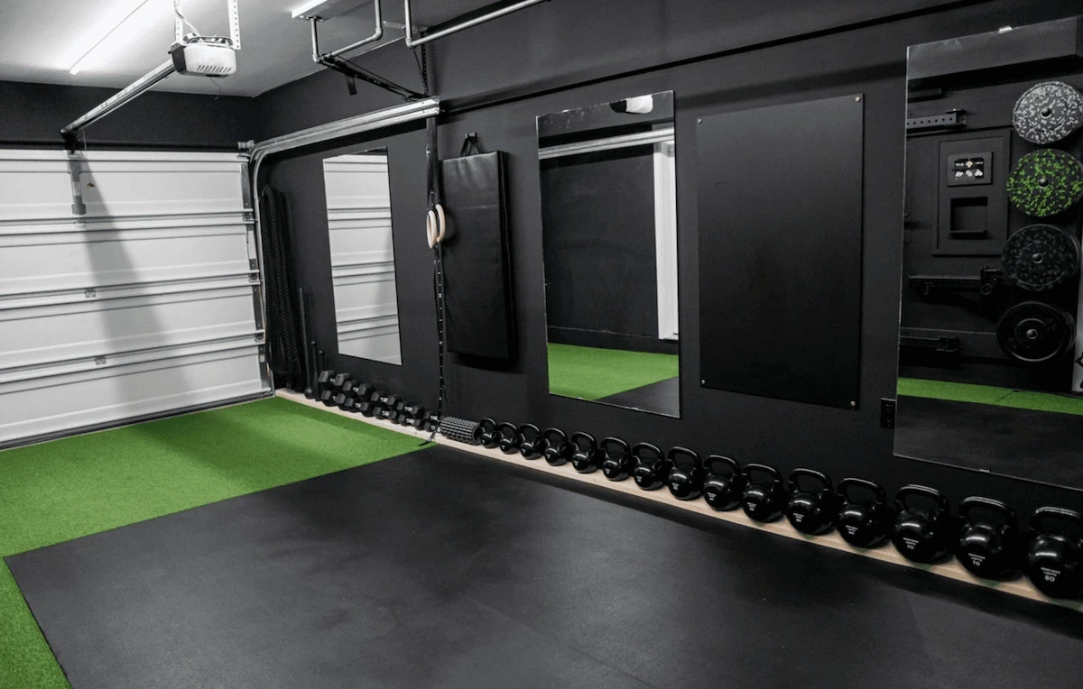 Garage home gym design in an Ottawa home featuring rubber flooring, turf training area, wall mirrors, and a streamlined layout for strength and mobility training