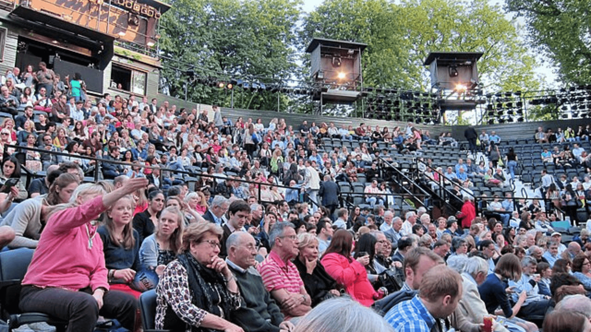 Audience members sitting in the outdoor raked seating at Regent's Park Open Air Theatre in London
