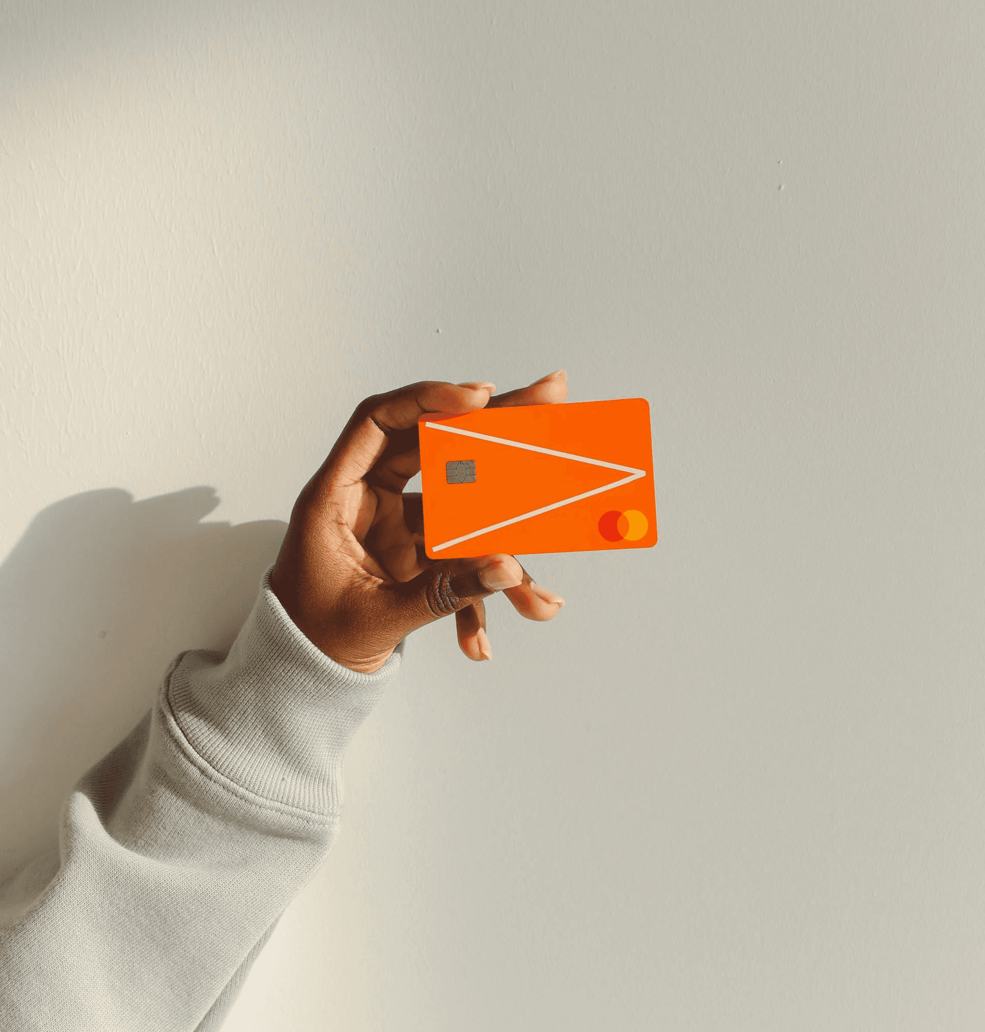 A hand holding an orange credit card high against a clear background