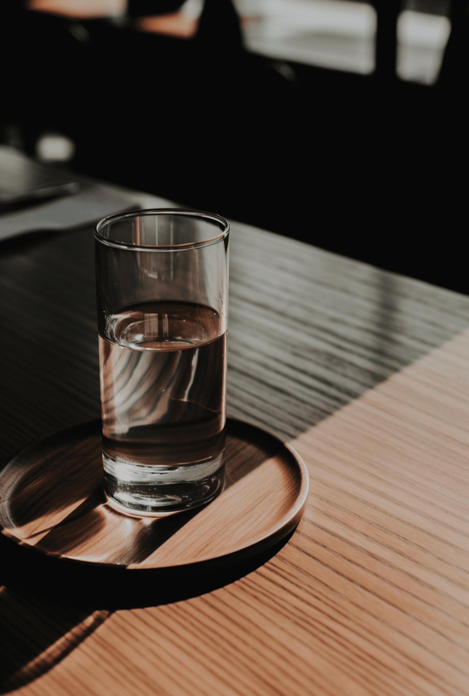 A glass of water on a wooden coaster, bathed in warm sunlight, casting shadows on a wooden table.