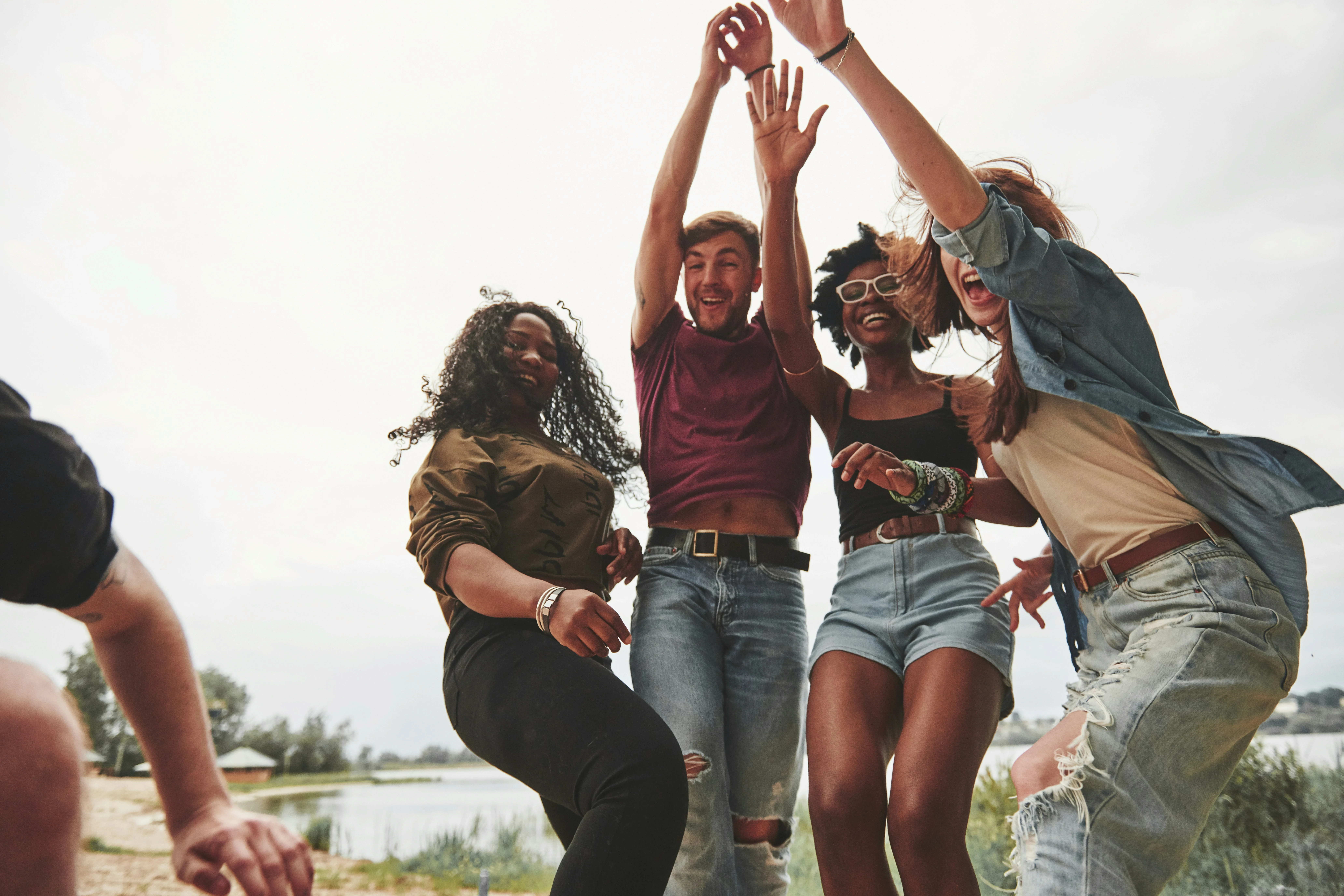 Diverse group of friends joyfully jumping outdoors by a lake, expressing connection, community, and celebration.