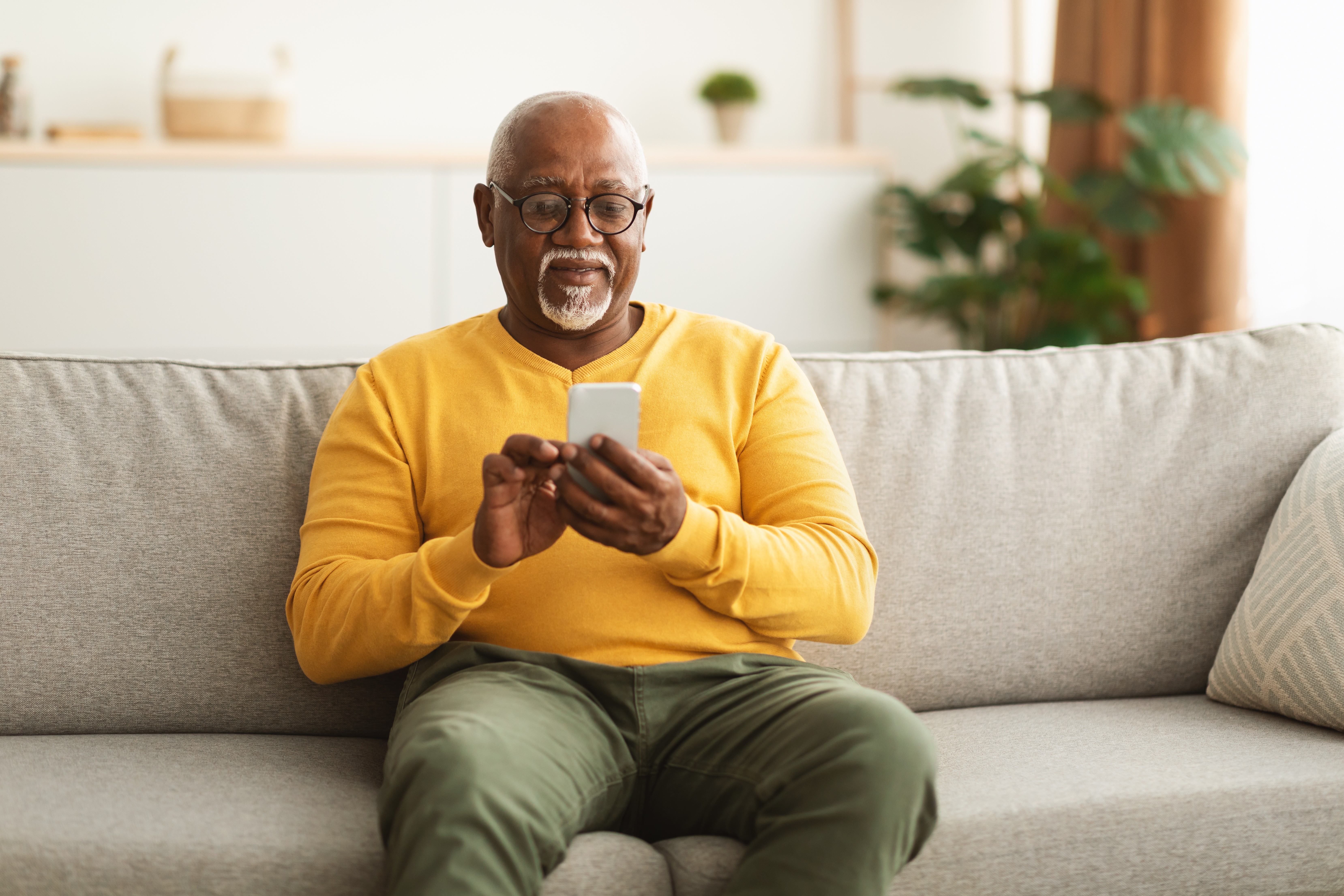 Older man sitting on a sofa looking at his phone - representing online pharmacy