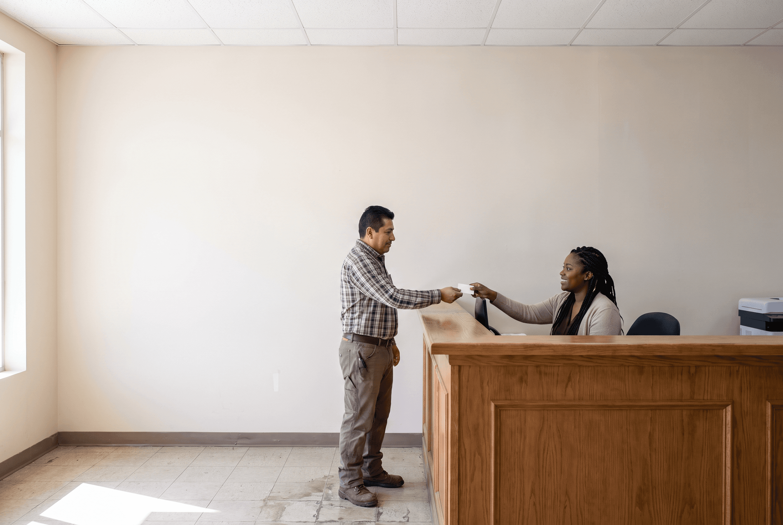 An employee handing a health plan ID card to the front desk at a doctor’s office