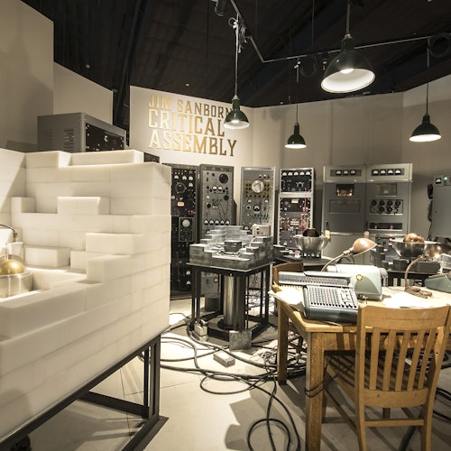 一個充滿復古科學設備的房間，包括控制面板、桌子上的打字機和一個大型白色幾何結構。