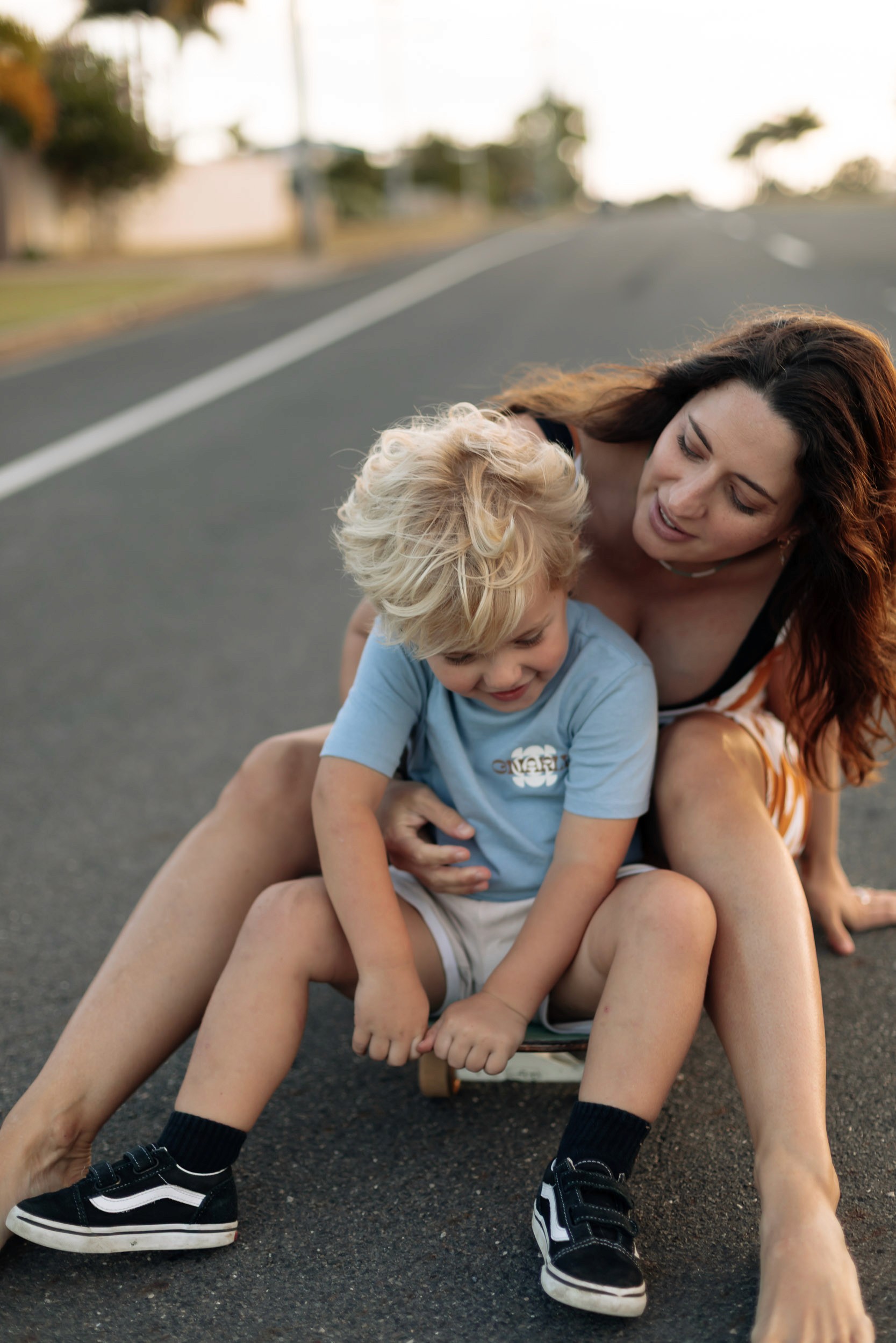 Mother skateboarding with her young child along a quiet road during a playful Mackay family photography session at sunset.