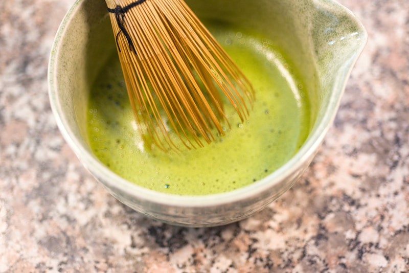 Matcha being whisked in a ceramic bowl with a bamboo chasen
